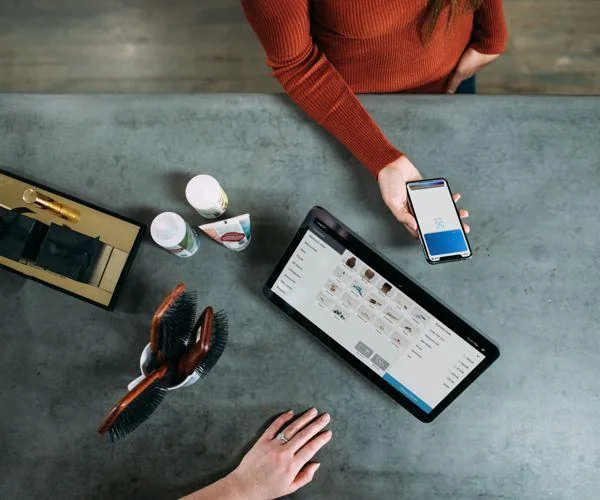 A shop counter seen from above: a phone showing the loyalty app in one hand, the till tablet beside it