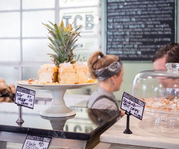 Handwritten price tags on a deli counter beside a cake stand