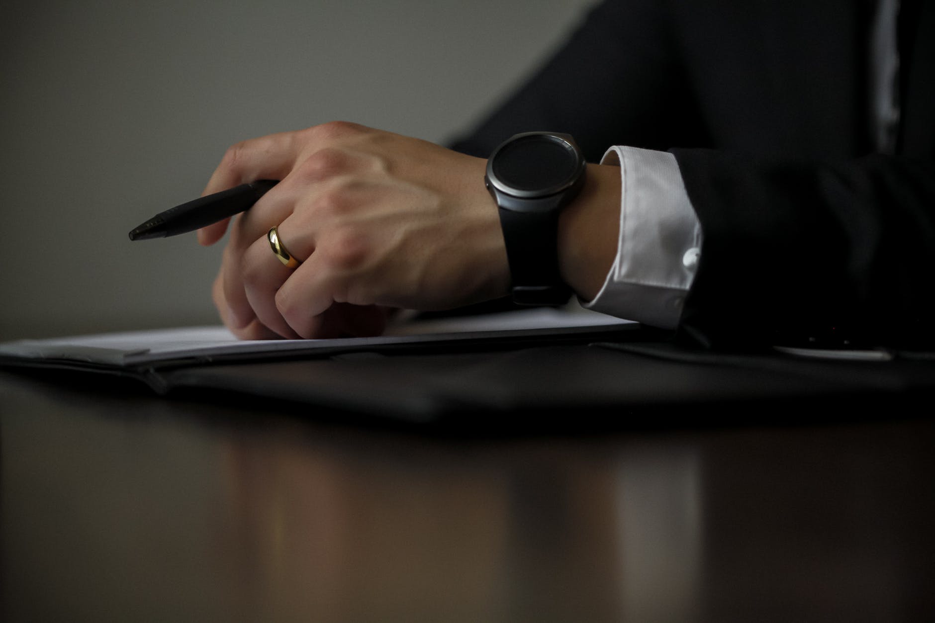 A hand with a pen resting on a signed contract at a dark desk