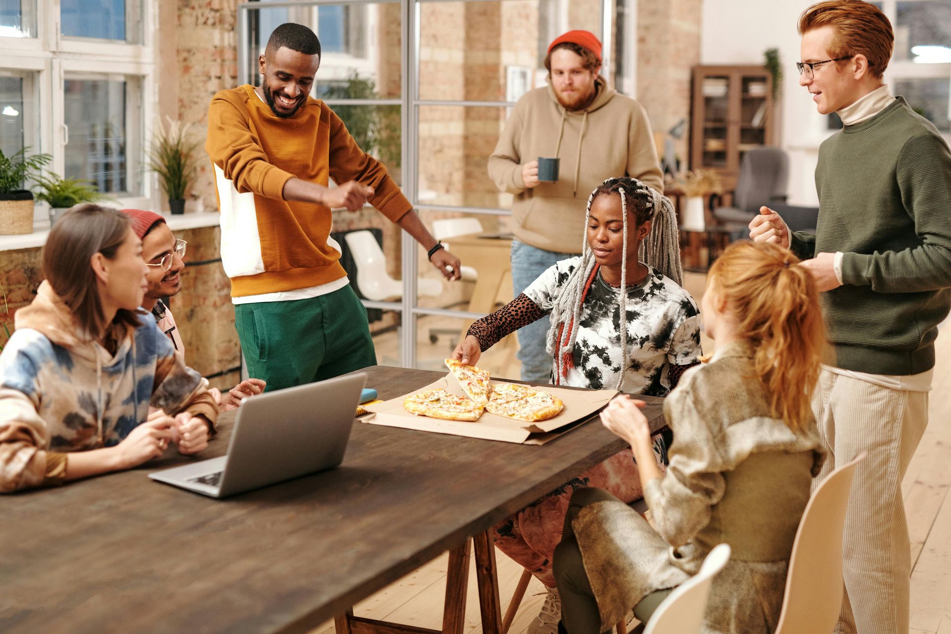 A team gathered around a long table sharing pizza beside an open laptop