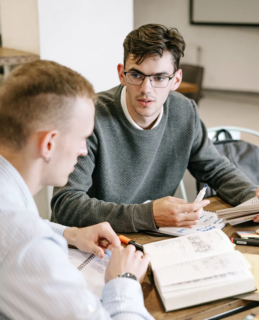 Two colleagues comparing notes over open notebooks at a shared desk